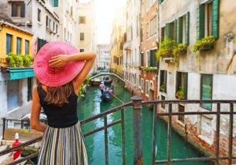 Frau mit rotem Sonnenhut schaut auf einen Kanal mit Gondel in Venedig, Italien