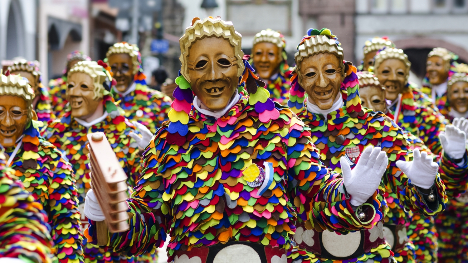 ©C. Schüßler - stock.adobe.com Menschen in bunten Trachten und Holzmasken bei einem traditionellen Festumzug.