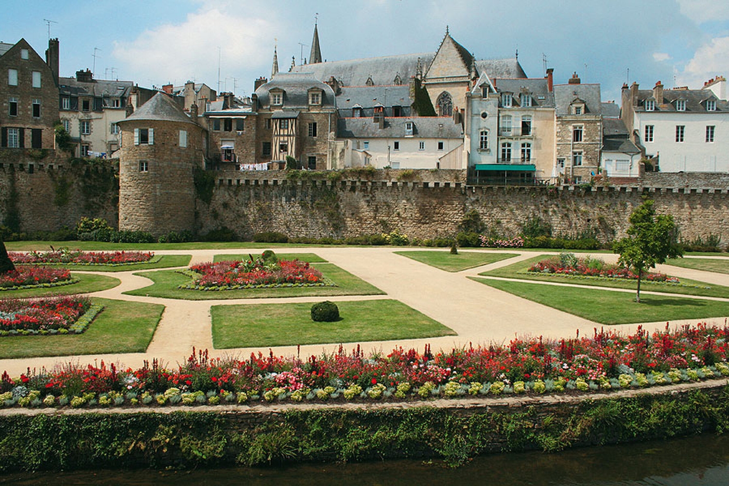Garten in Vannes mit Blumenbeeten vor alten Stadtmauern und historischen Gebäuden.