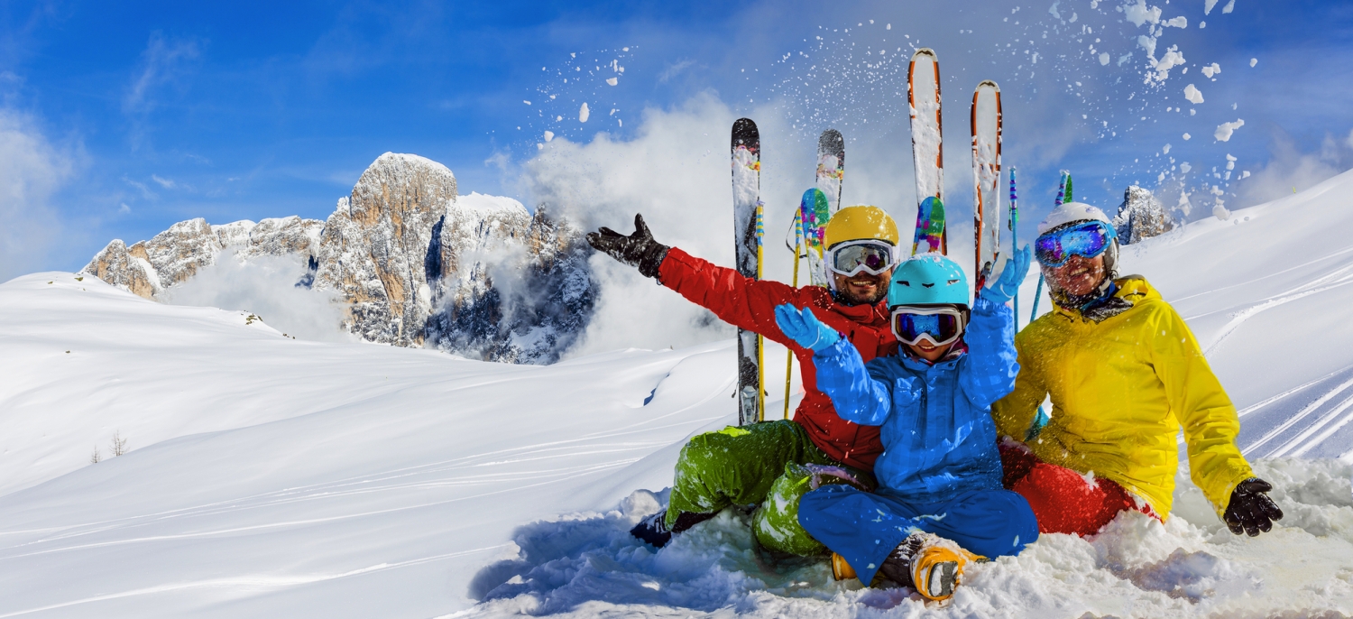 Familie im Schnee beim Skifahren in den Alpen mit strahlend blauem Himmel.