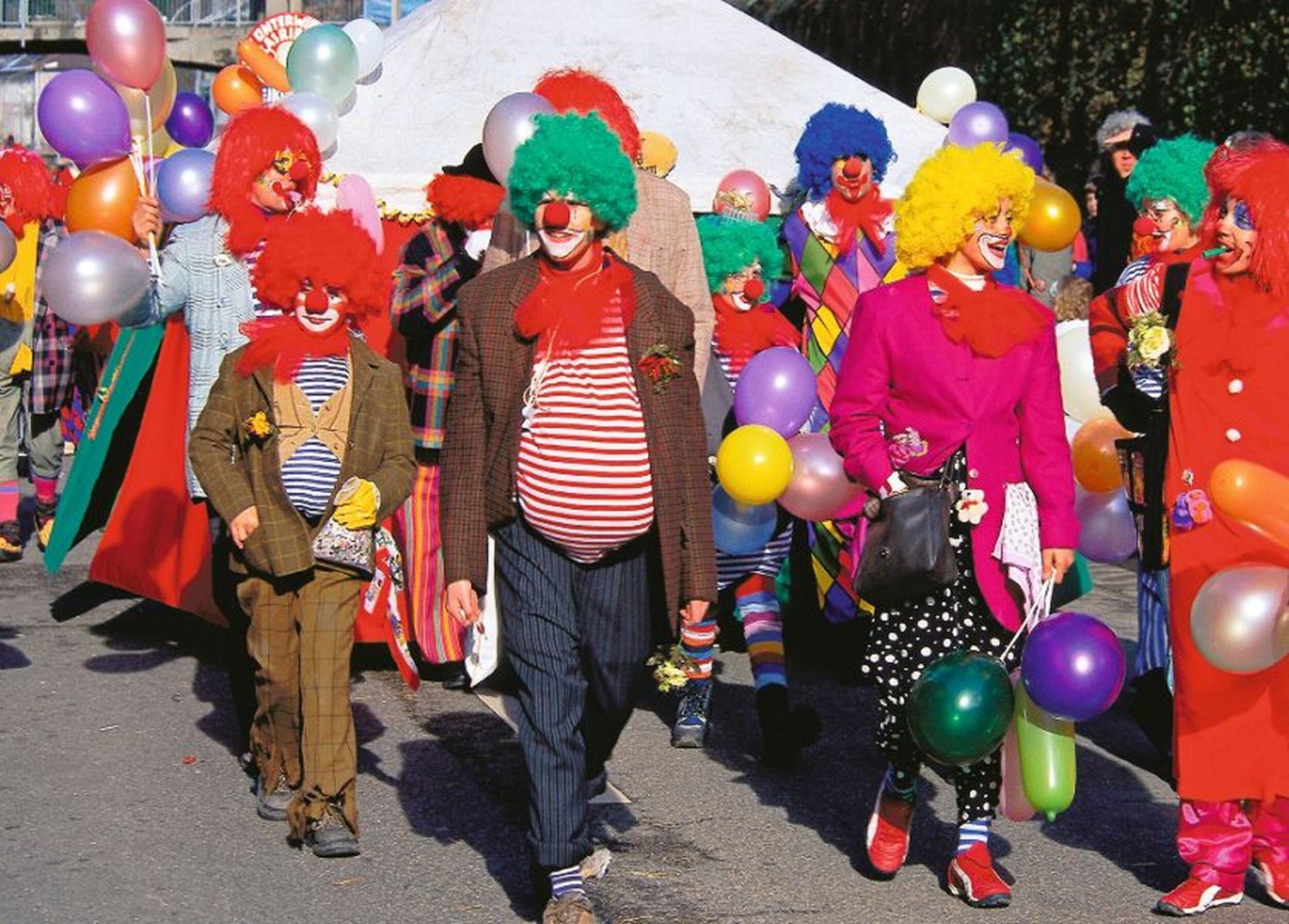 Menschen in bunten Clownskostümen mit Luftballons auf einem Karnevalsumzug.