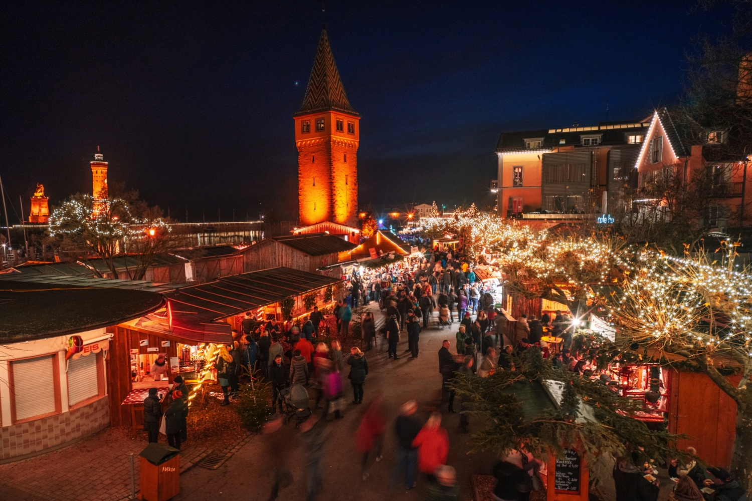 © J.M. Soedher Menschen auf einem festlich beleuchteten Weihnachtsmarkt bei Nacht.