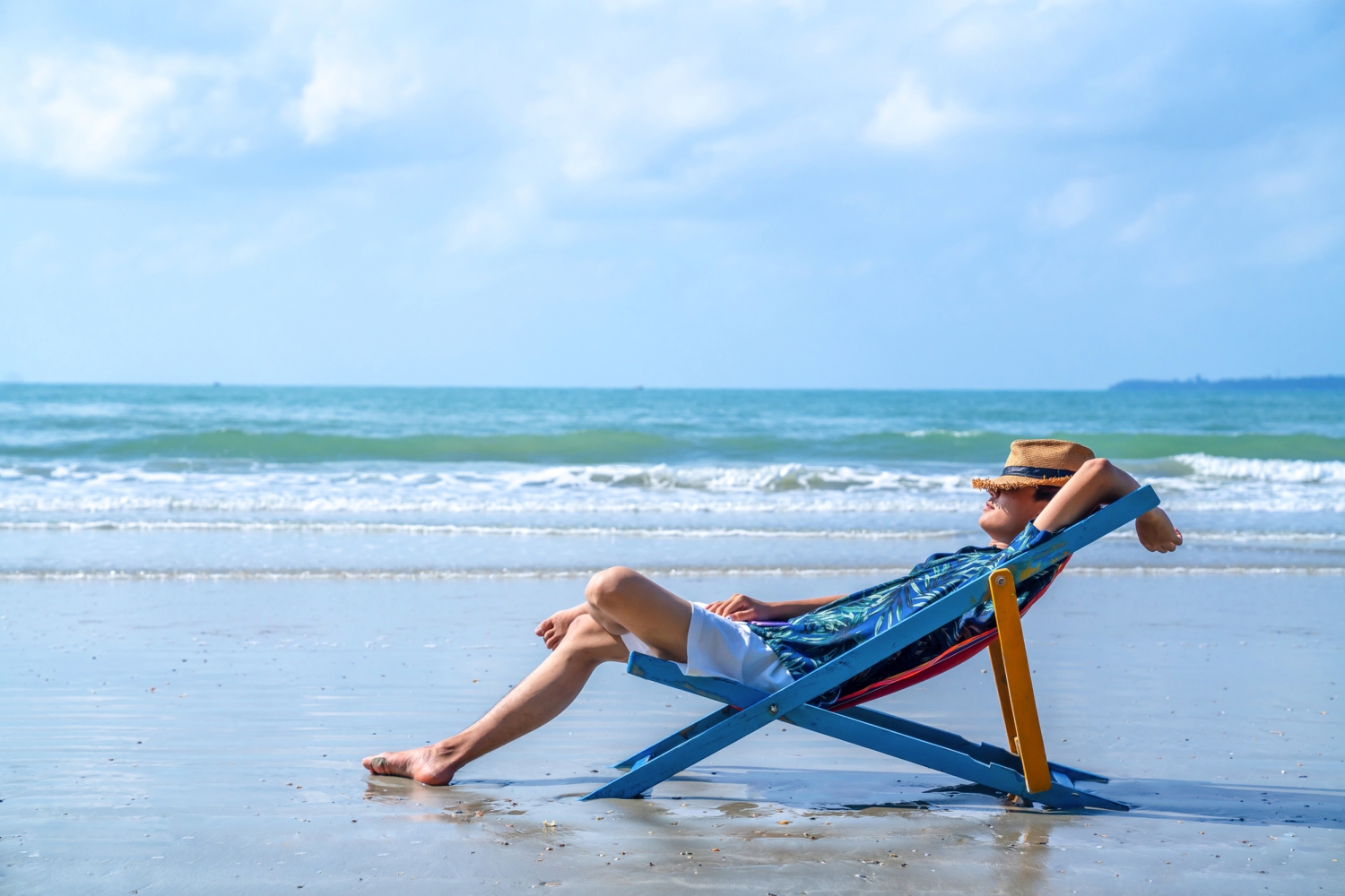 © CandyRetriever - stock.adobe.com Person entspannt auf Liegestuhl am Strand unter blauem Himmel.