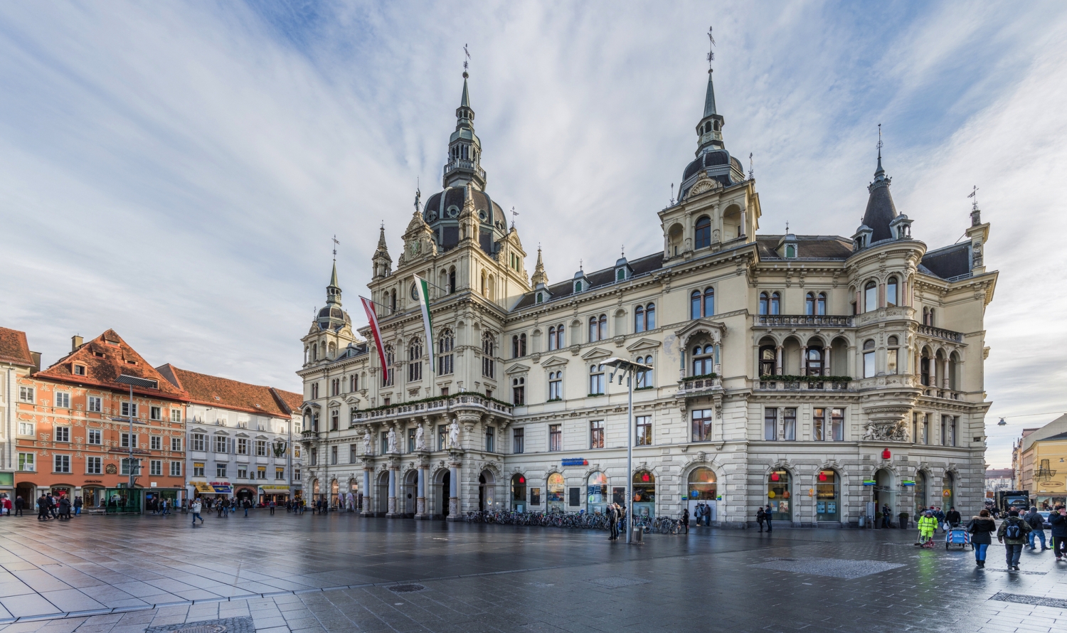 Historisches Gebäude an einem belebten Platz mit Menschen und blauem Himmel.