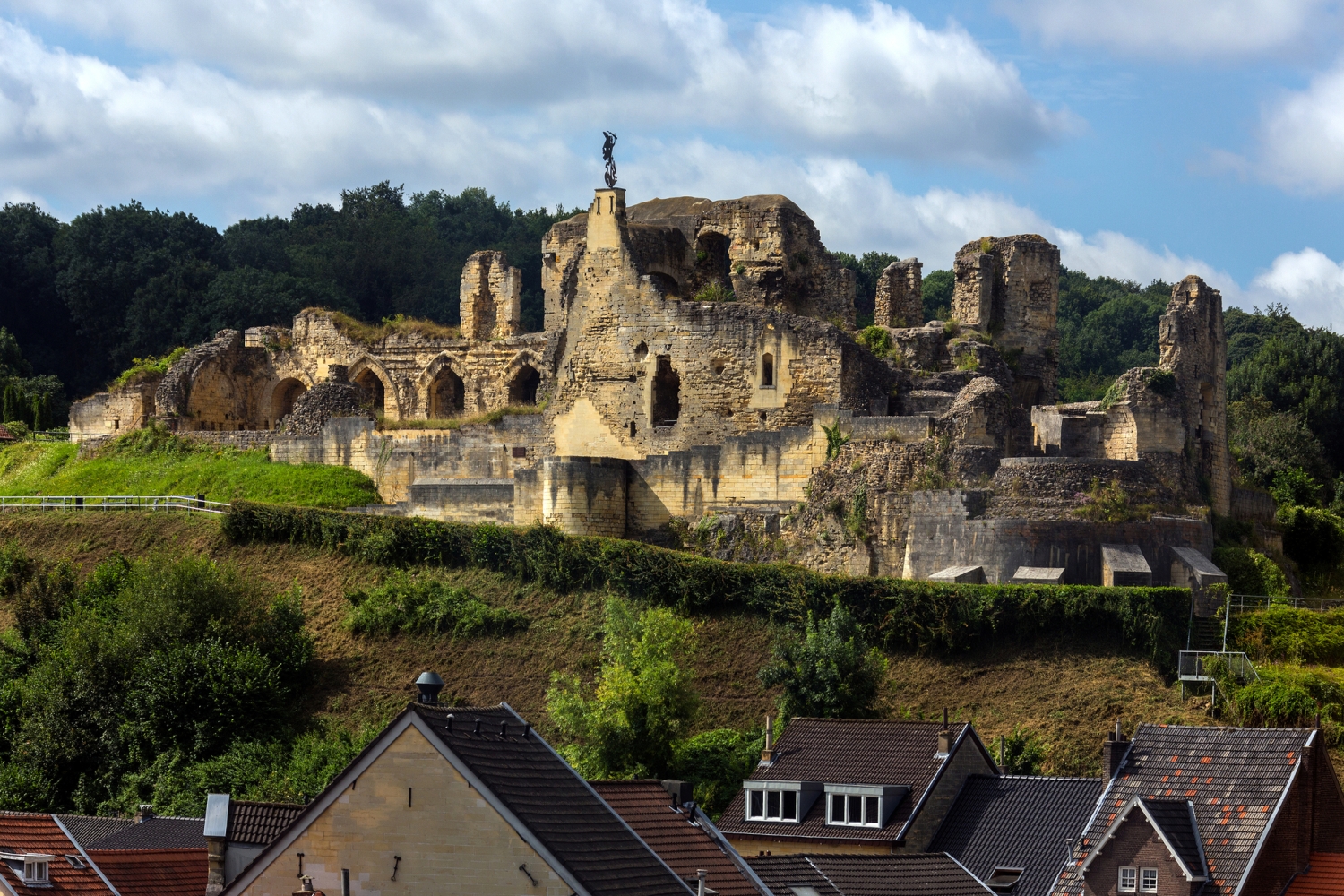 Ruine einer Burg auf einem Hügel, umgeben von Häusern und Bäumen.