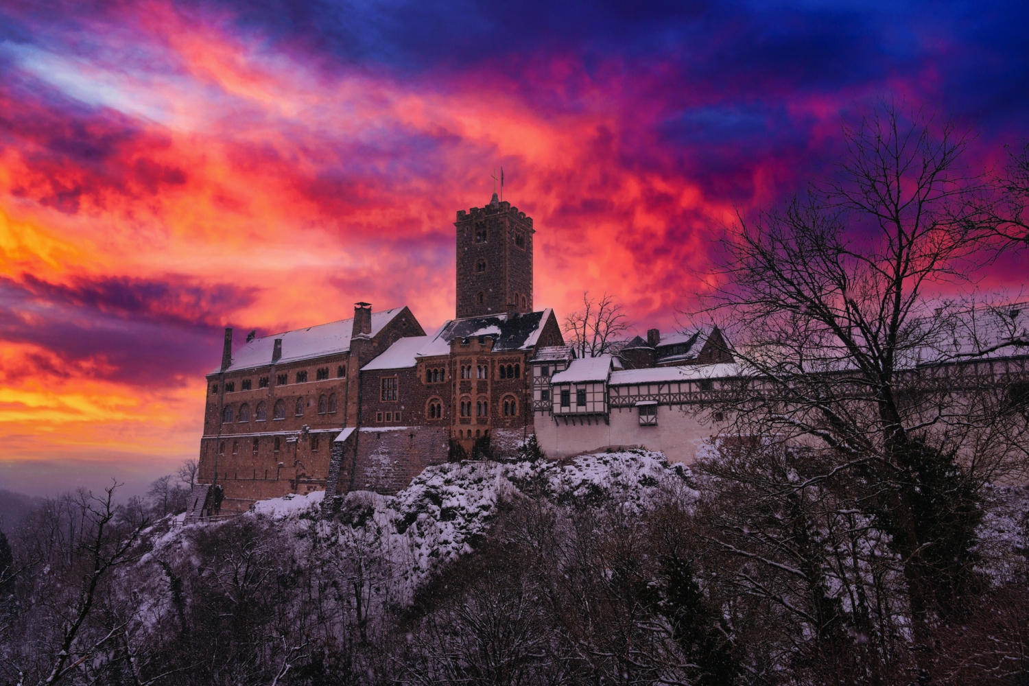 Mittelalterliche Burg im Winter, umgeben von Bäumen, vor farbigem Sonnenuntergang.