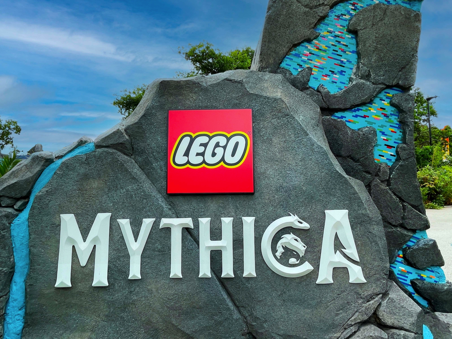 Steinschild mit LEGO-Mythica-Logo vor blauem Himmel.