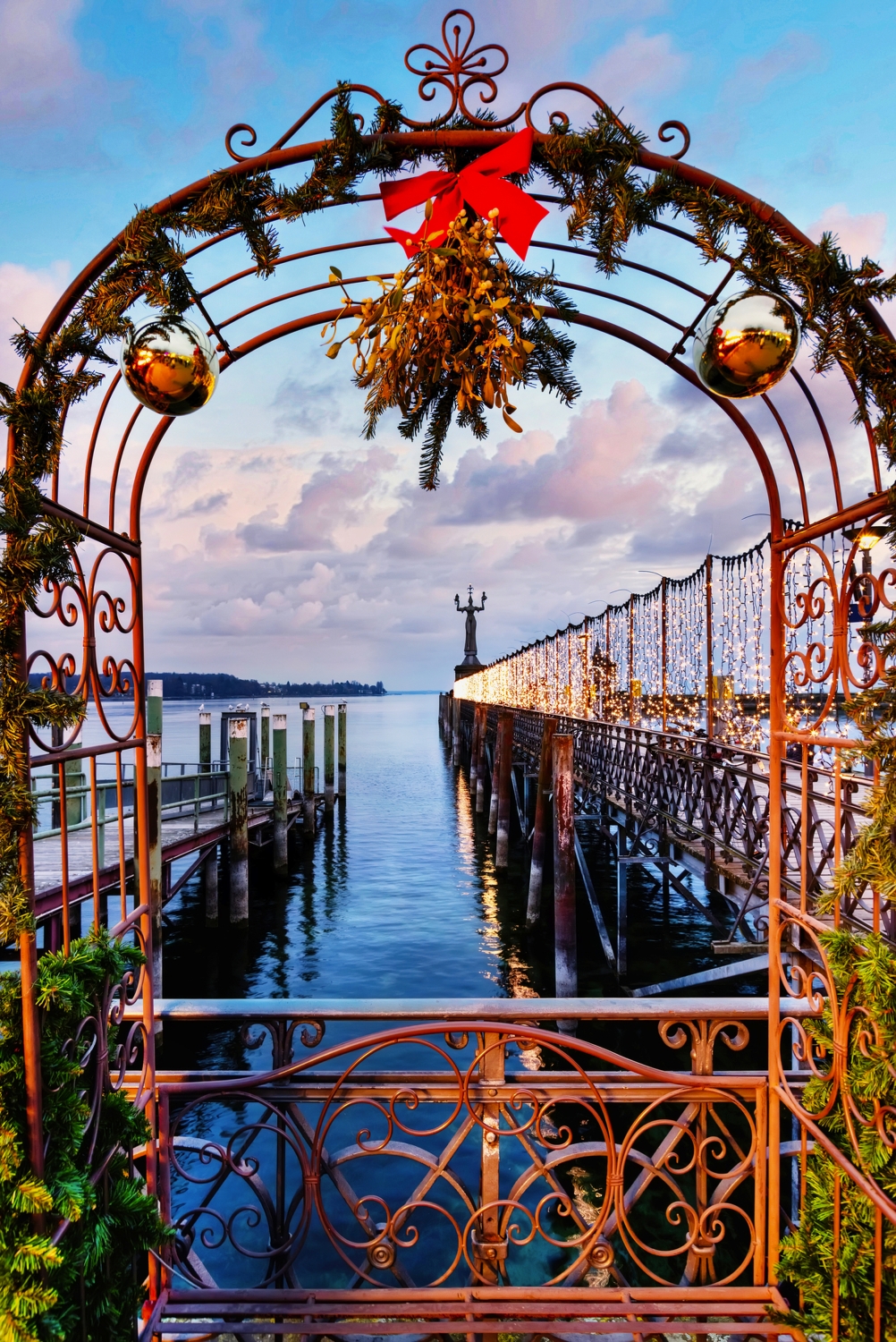 © EKH-Pictures - stock.adobe.com Bogen mit weihnachtlicher Dekoration vor einem Steg über Wasser bei Sonnenuntergang.