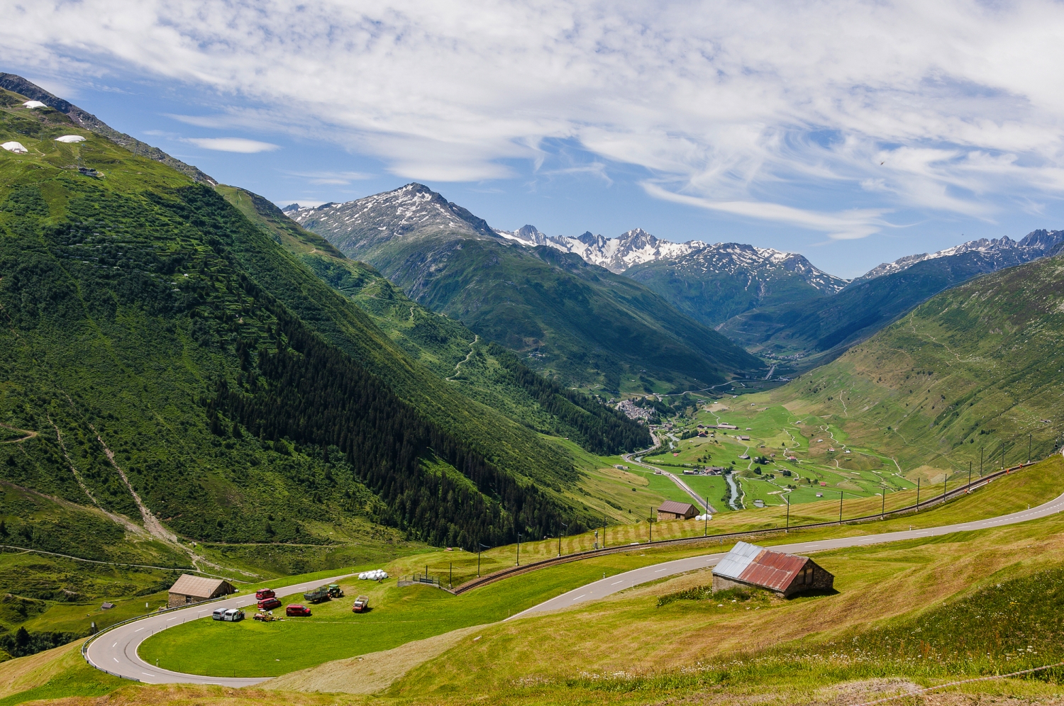 Berglandschaft mit grünen Tälern und schneebedeckten Gipfeln im Hintergrund.