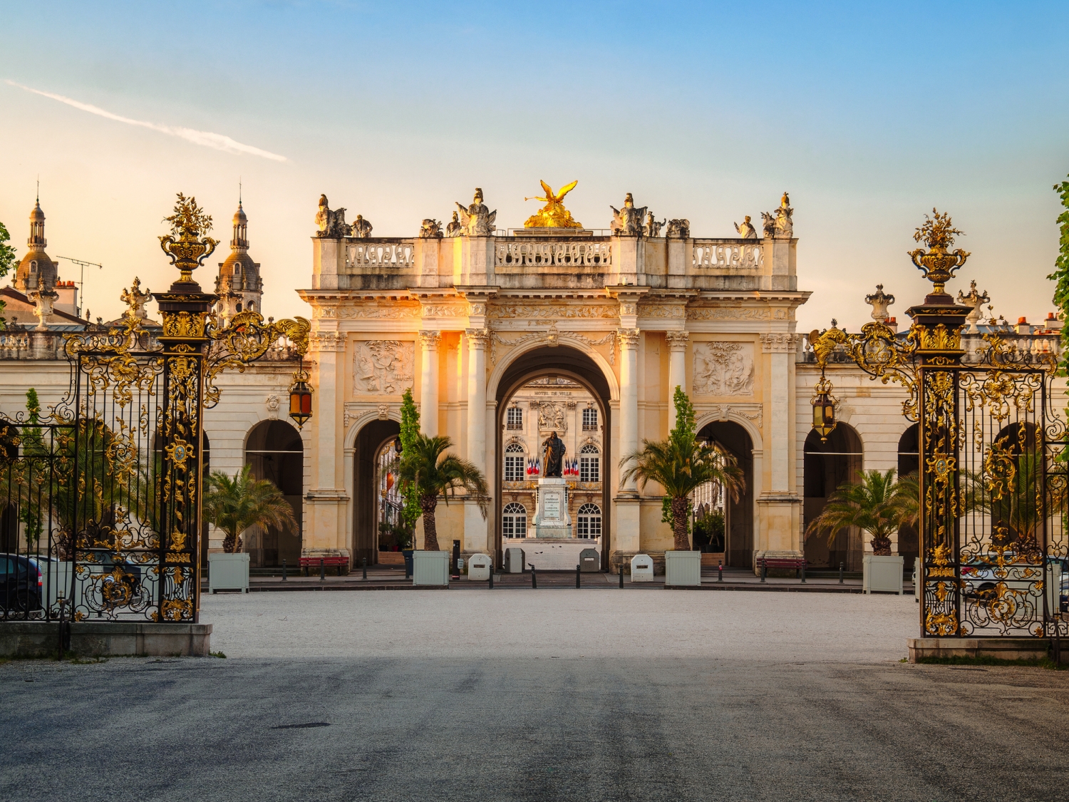 Monumentales Tor mit Verzierungen und Gebäude im Hintergrund bei Sonnenuntergang.