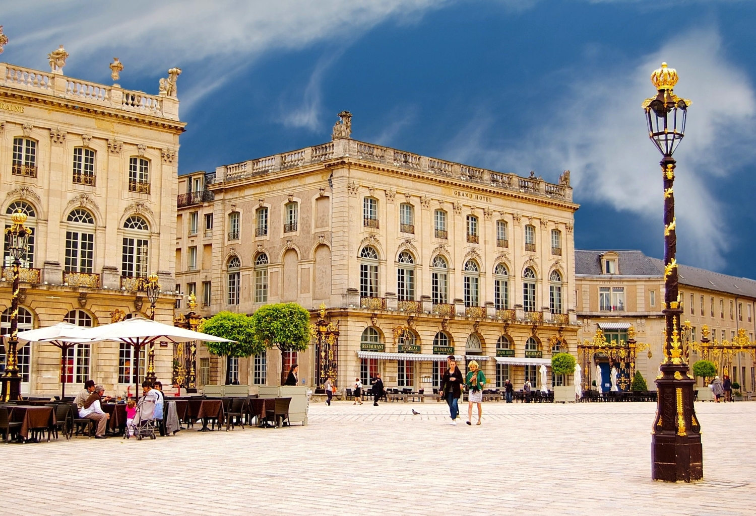 Historischer Platz mit Barockgebäuden und Menschen unter Sonnenschirmen.