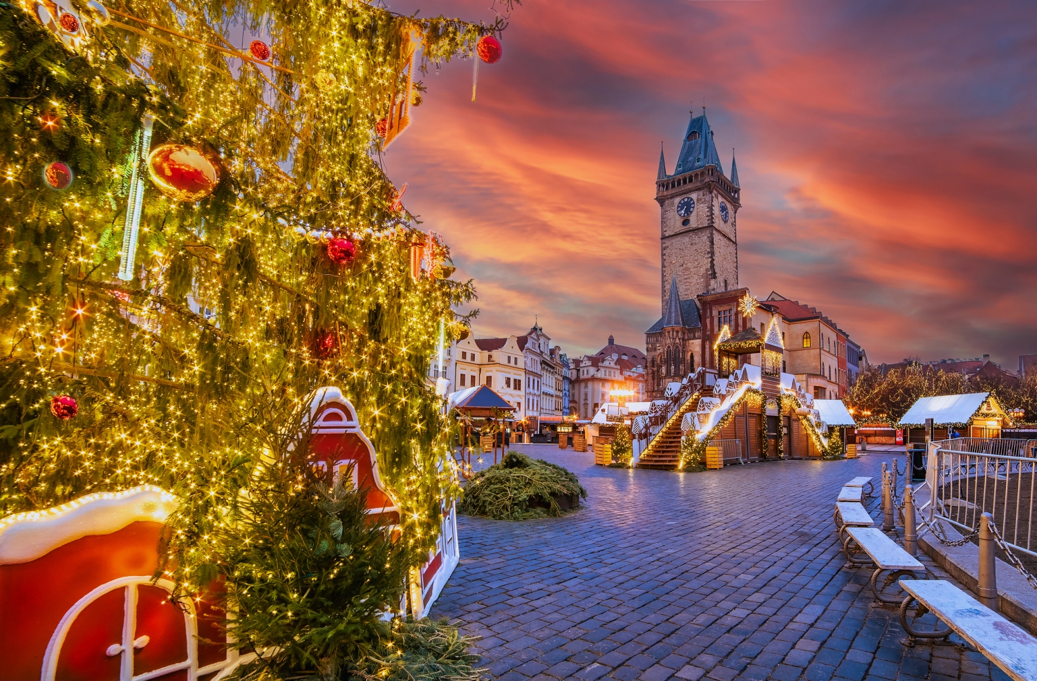 Weihnachtsmarkt bei Sonnenuntergang mit Weihnachtsbaum und Uhrenturm im Hintergrund