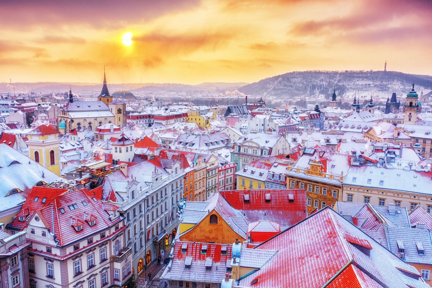 Stadtansicht im Winter mit verschneiten Dächern und orange-violettem Sonnenuntergang.