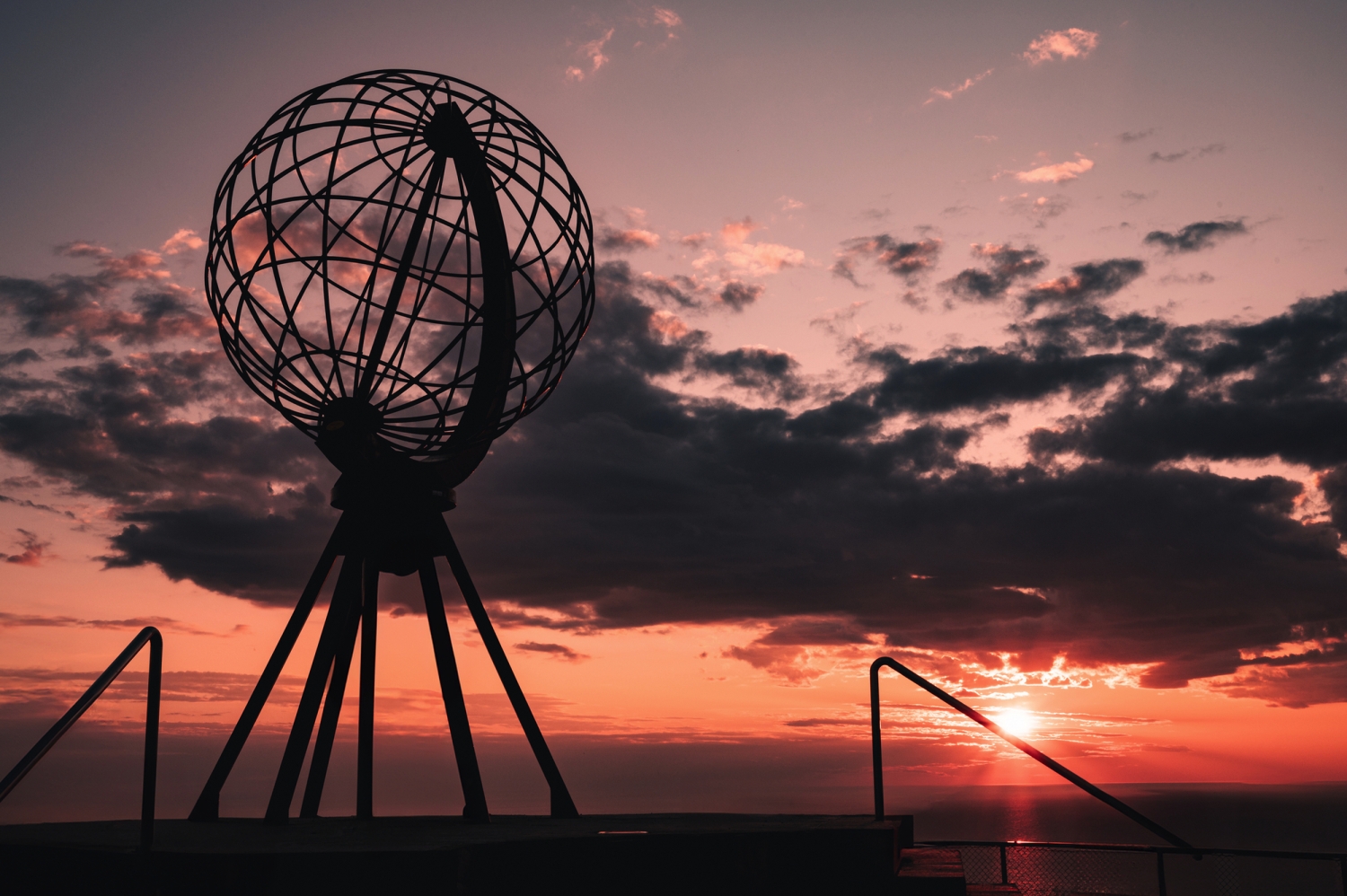 Skulptur eines Globus bei Sonnenuntergang am Meer.