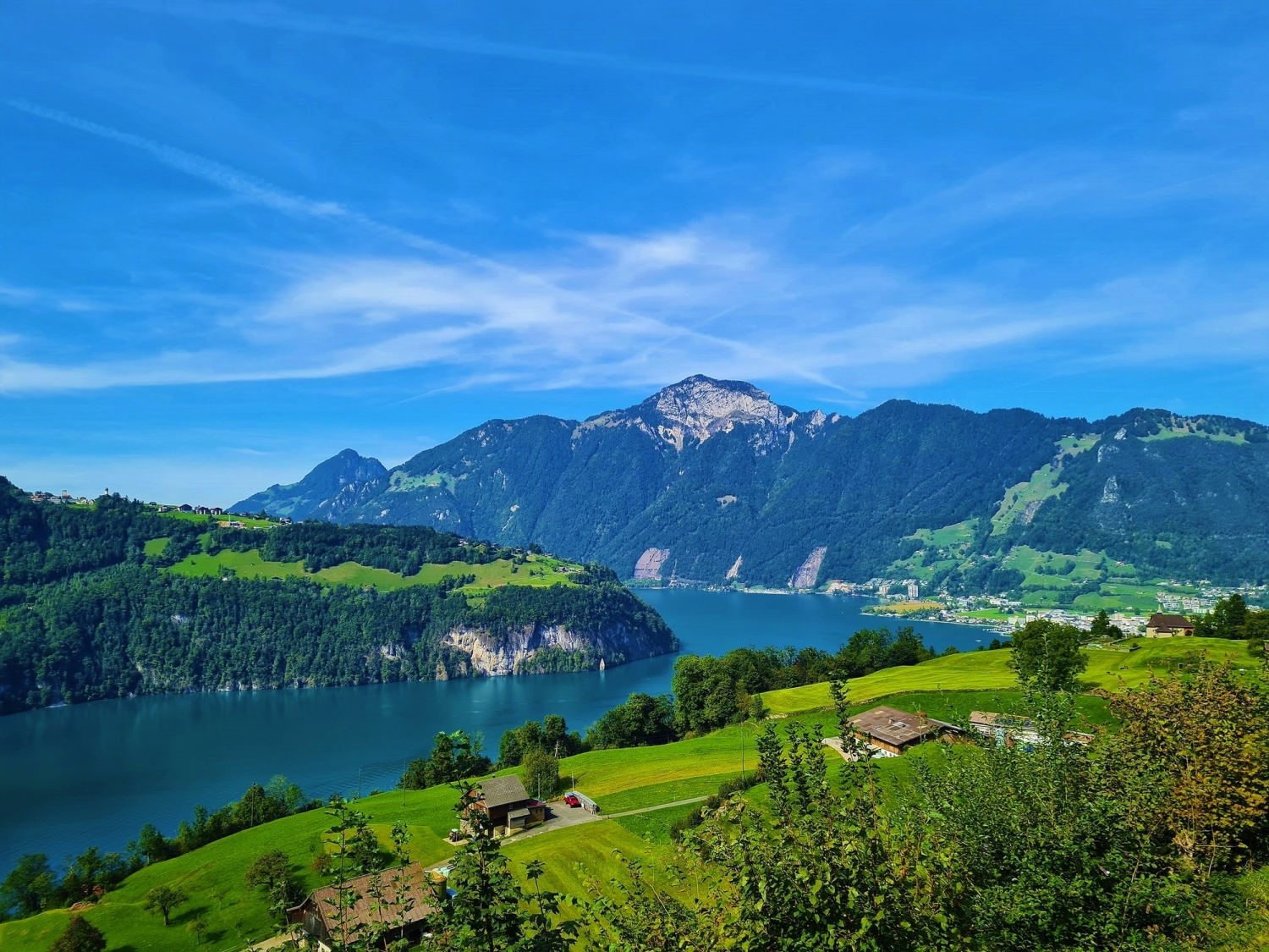 Landschaft mit See, Bergen und grünem Tal unter blauem Himmel.