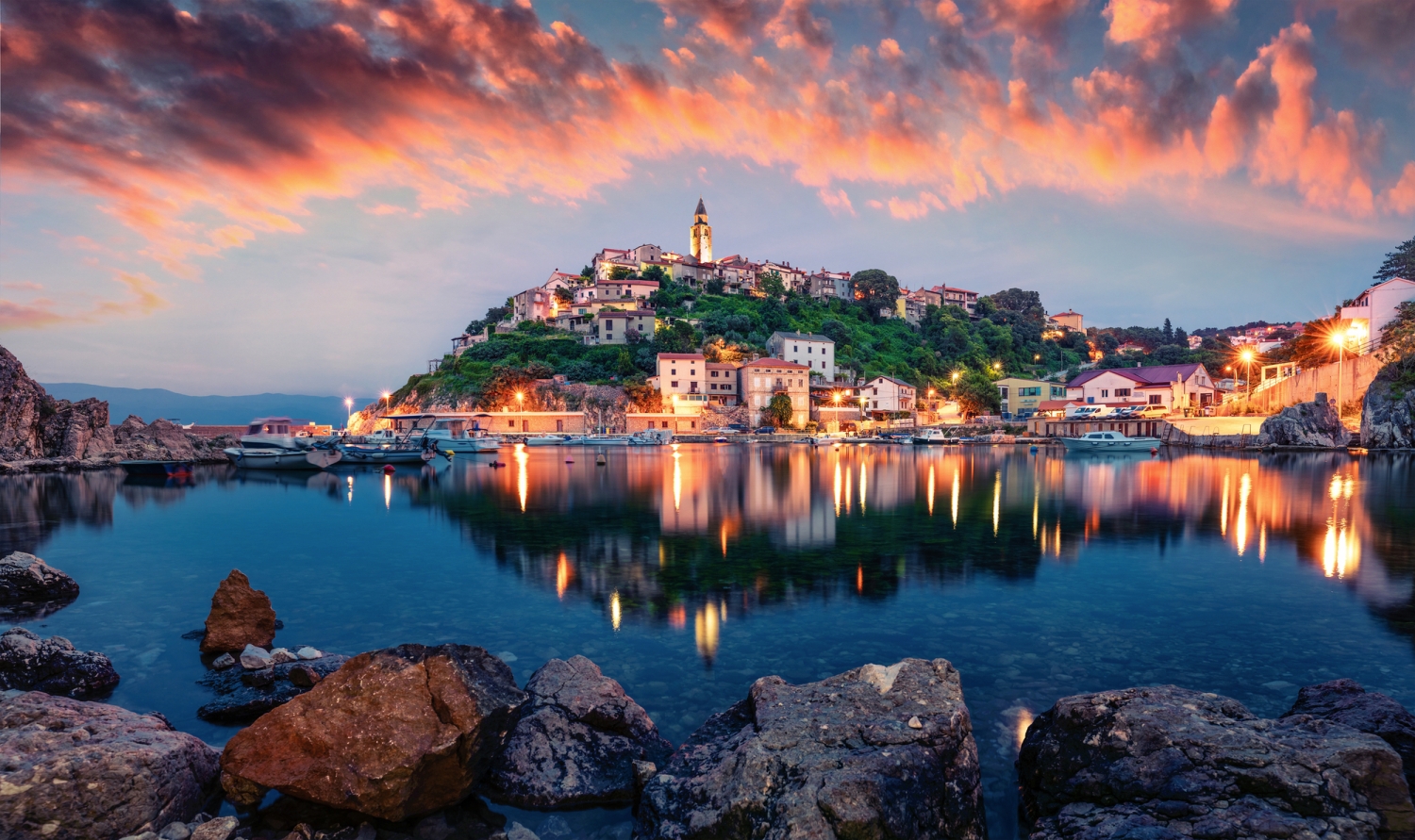 Küstenstadt bei Sonnenuntergang, spiegelnd im ruhigen Wasser.