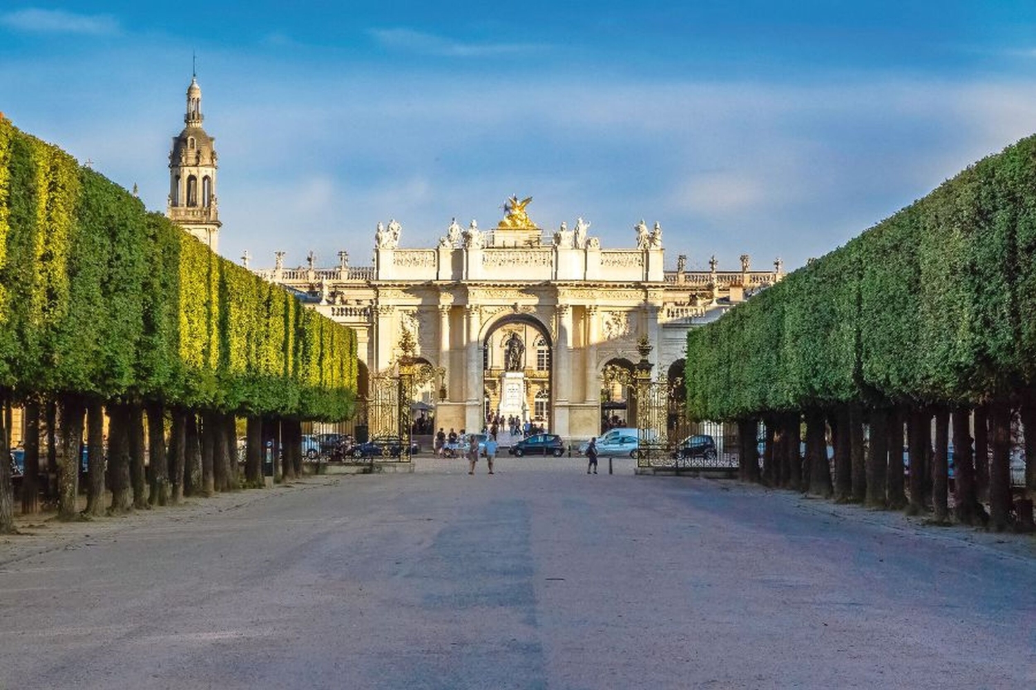 Weg mit Bäumen und Blick auf einen prachtvollen Torbogen bei blauem Himmel.