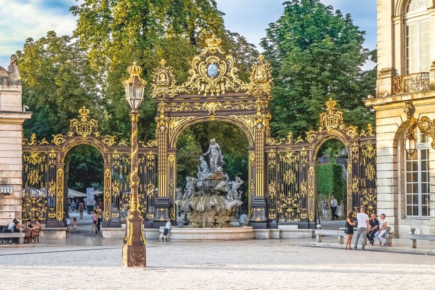 Verzierte Torbögen und Brunnen auf einem Platz mit Menschen im Hintergrund.