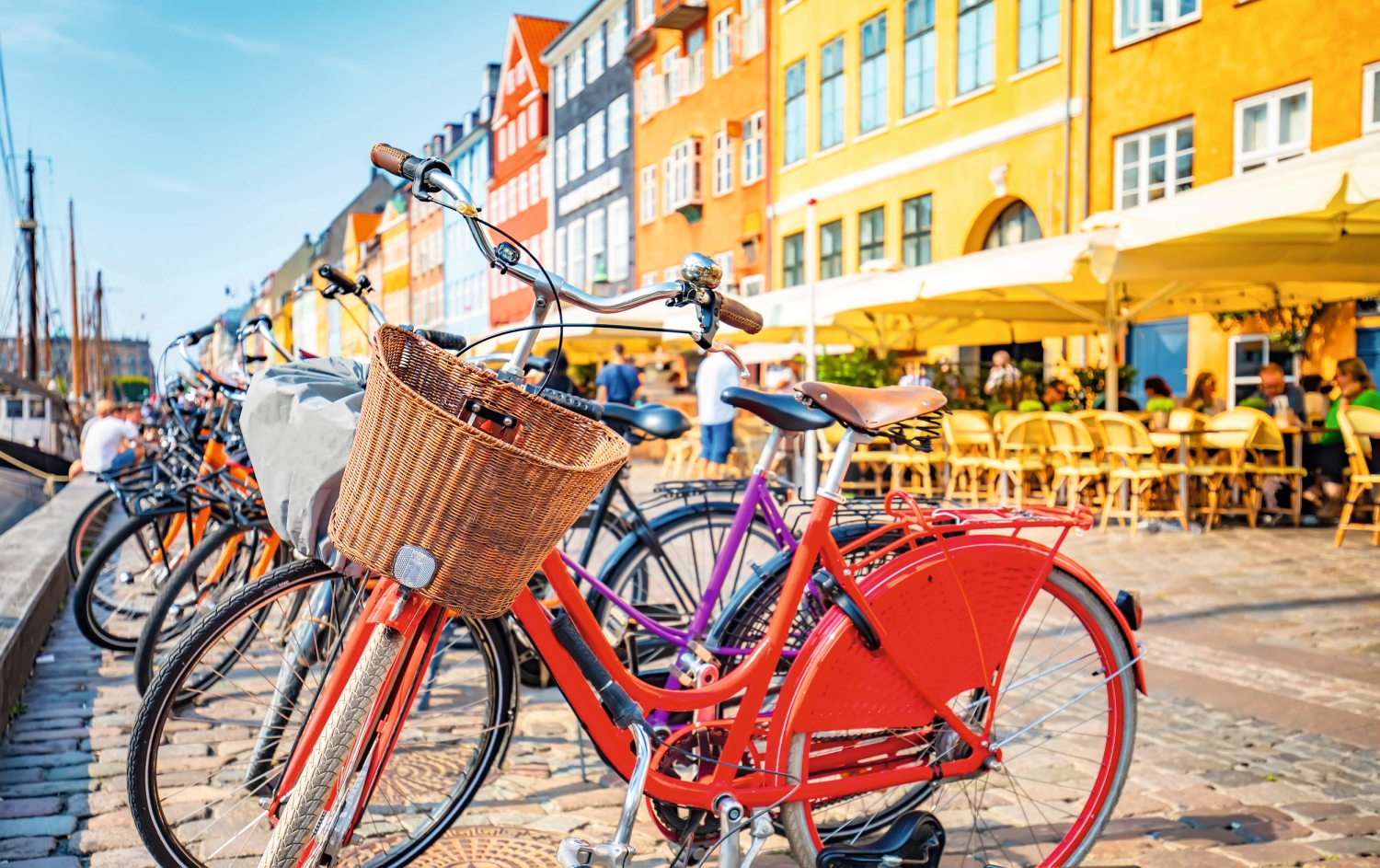 Fahrräder am Kai einer bunten, sonnigen Hafenstraße mit Café in der Nähe.