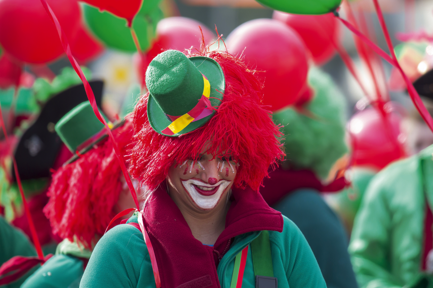 © Gerhard Bittner - Fotolia Person in Clownkostüm mit roten Luftballons und rotem Haar bei einer Parade