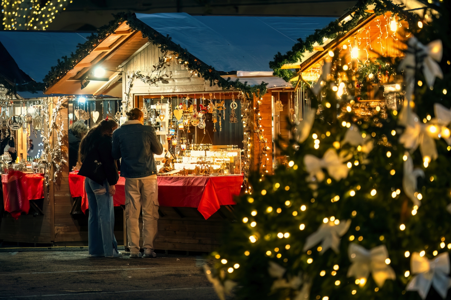 Menschen kaufen an Ständen auf einem festlich beleuchteten Weihnachtsmarkt ein.