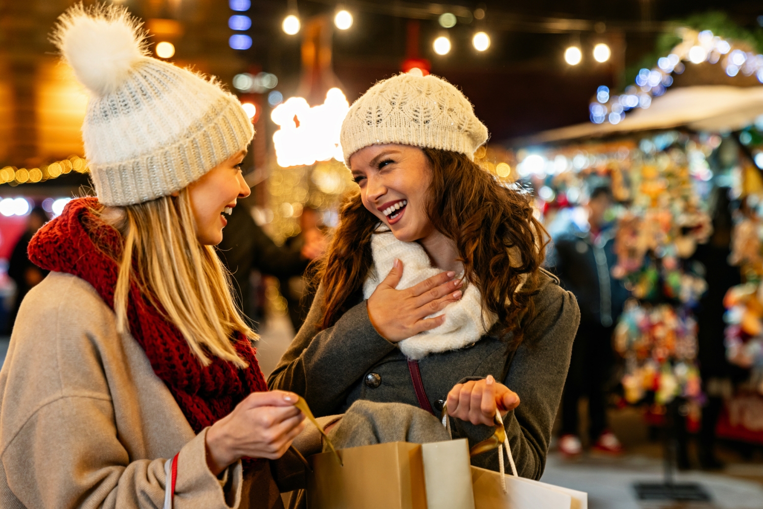 Zwei lachende Frauen mit Einkaufstaschen auf einem Weihnachtsmarkt.
