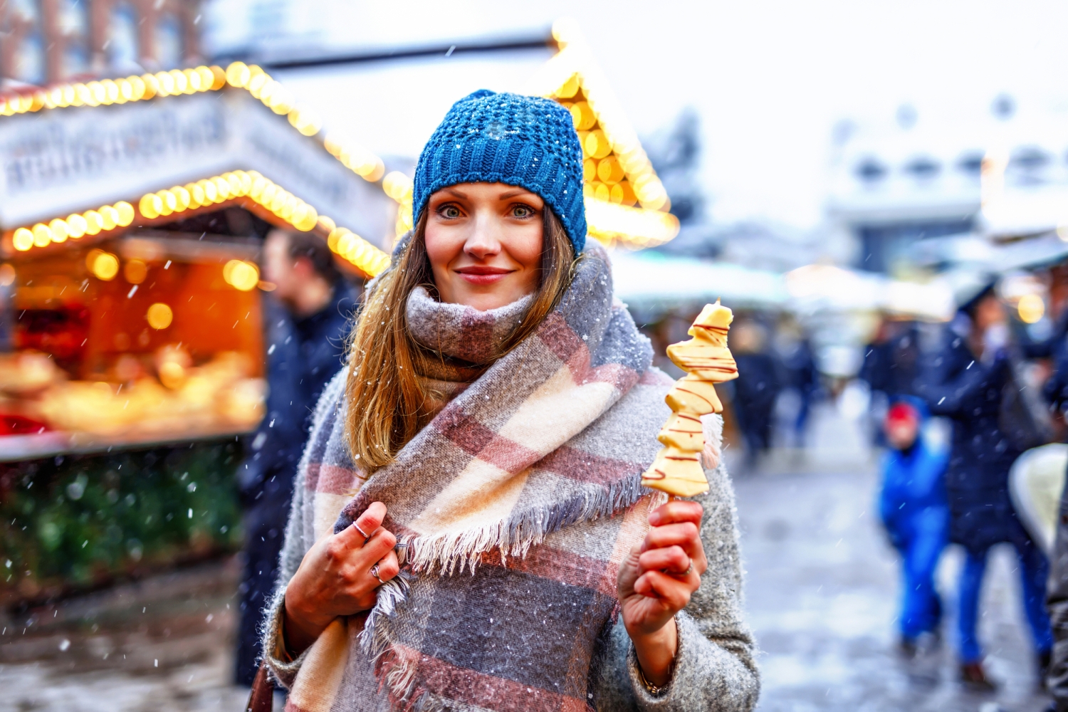 Frau mit blauer Mütze genießt gebratene Pilze auf einem Wintermarkt bei Schnee.