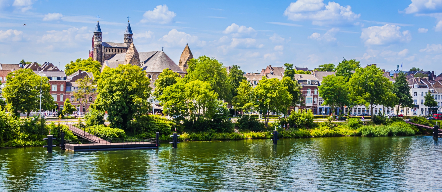 Stadtansicht mit Kirche und Fluss unter blauem Himmel.