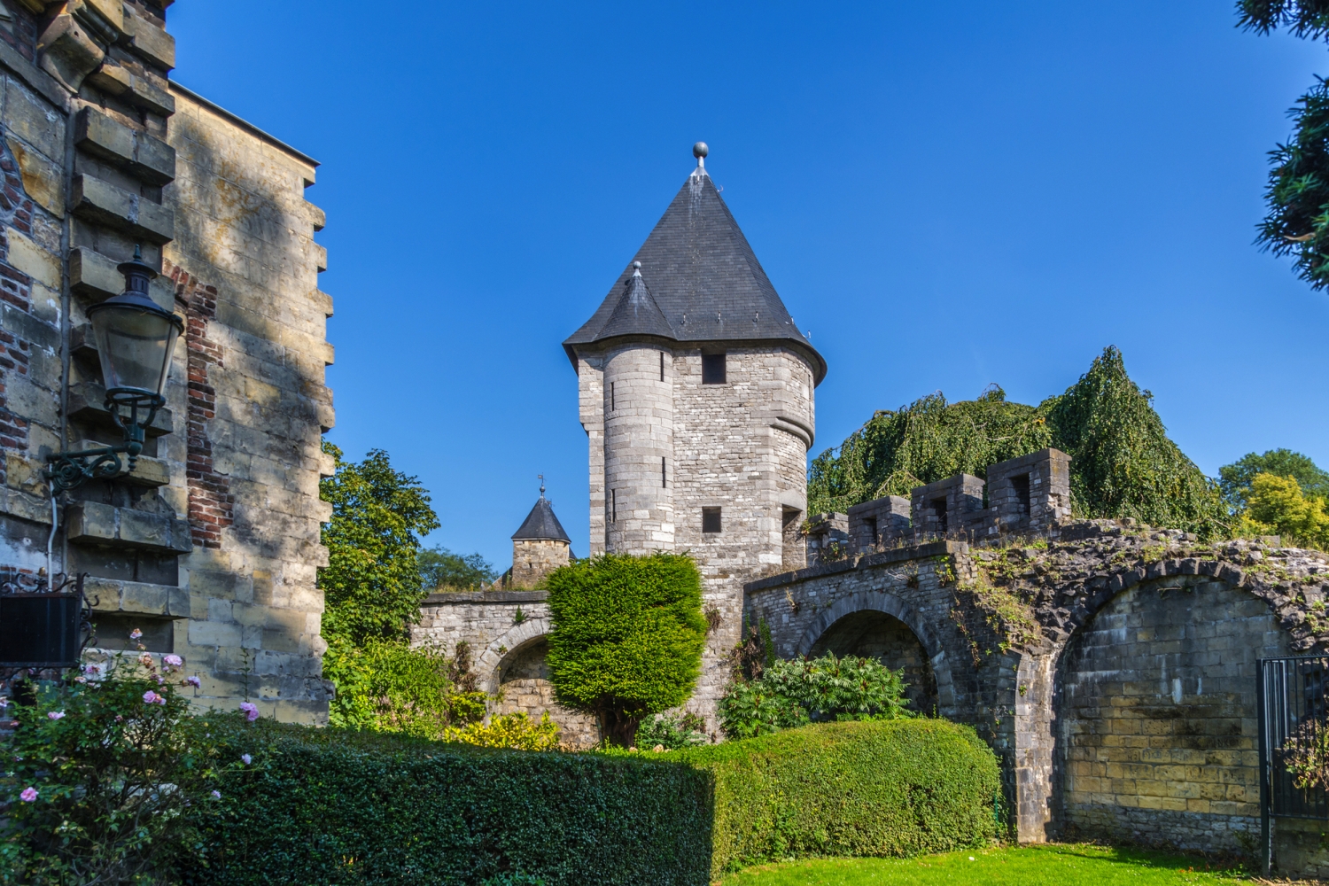 Mittelalterlicher Turm und Stadtmauer mit grünem Garten und blauem Himmel.