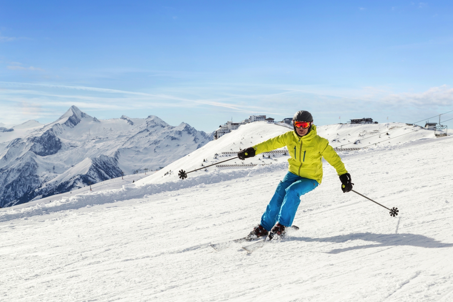 Skifahrer in bunter Kleidung auf schneebedecktem Berg mit blauen Himmel im Hintergrund.