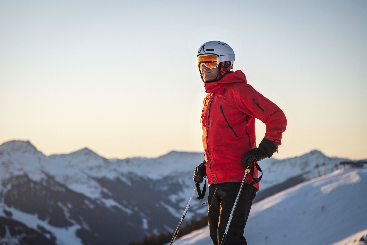 Skifahrer in roter Jacke blickt von schneebedecktem Bergpanorama.