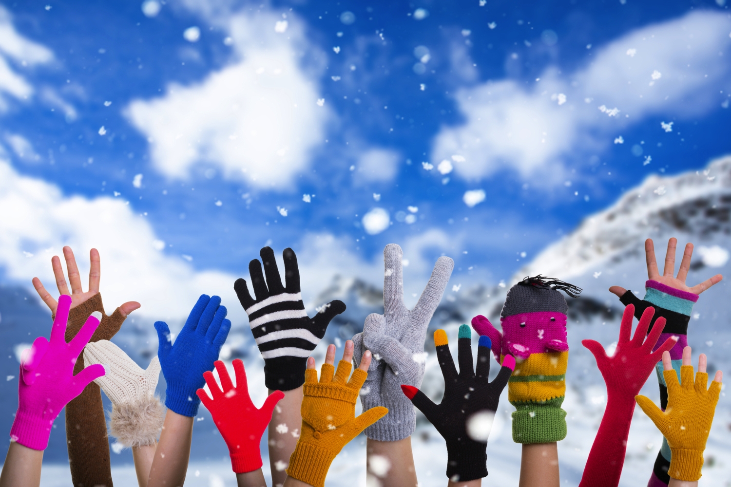 Verschiedene bunte Handschuhe in die Luft gestreckt vor verschneitem Hintergrund