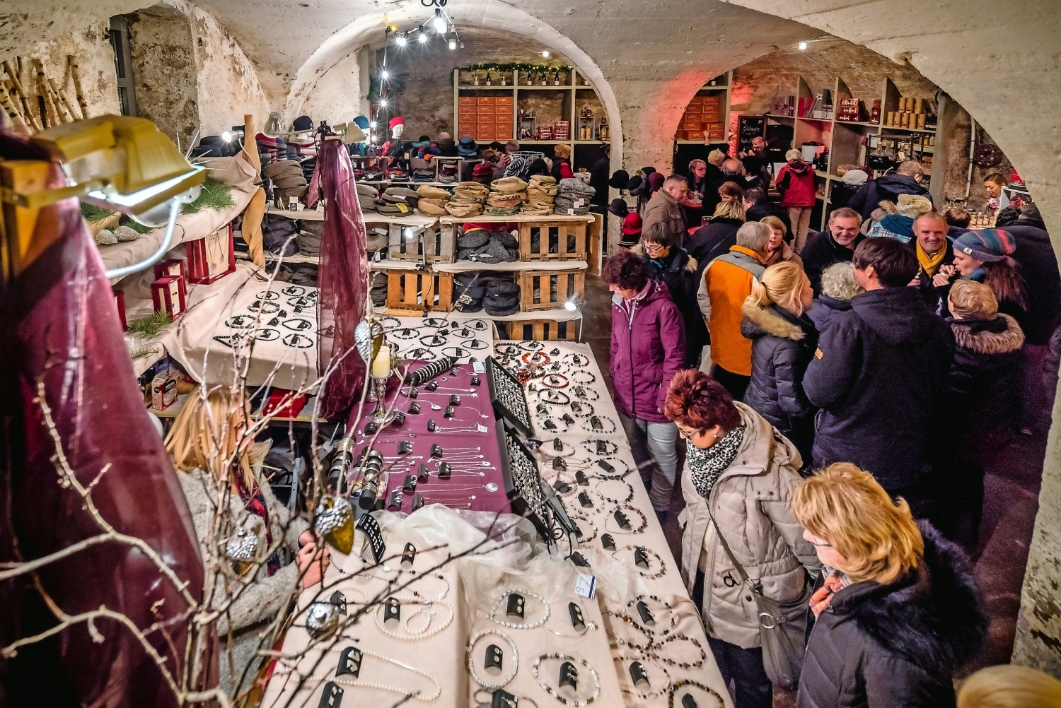 Menschen besuchen einen Handwerksmarkt in einem Gewölbekeller.