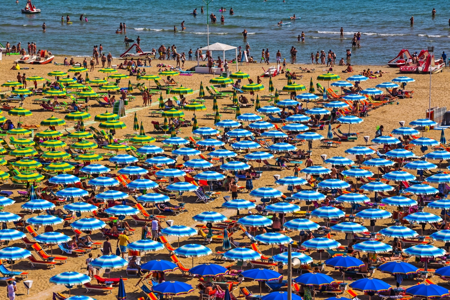 Strand mit zahlreichen bunten Sonnenschirmen und Menschen am Meer.