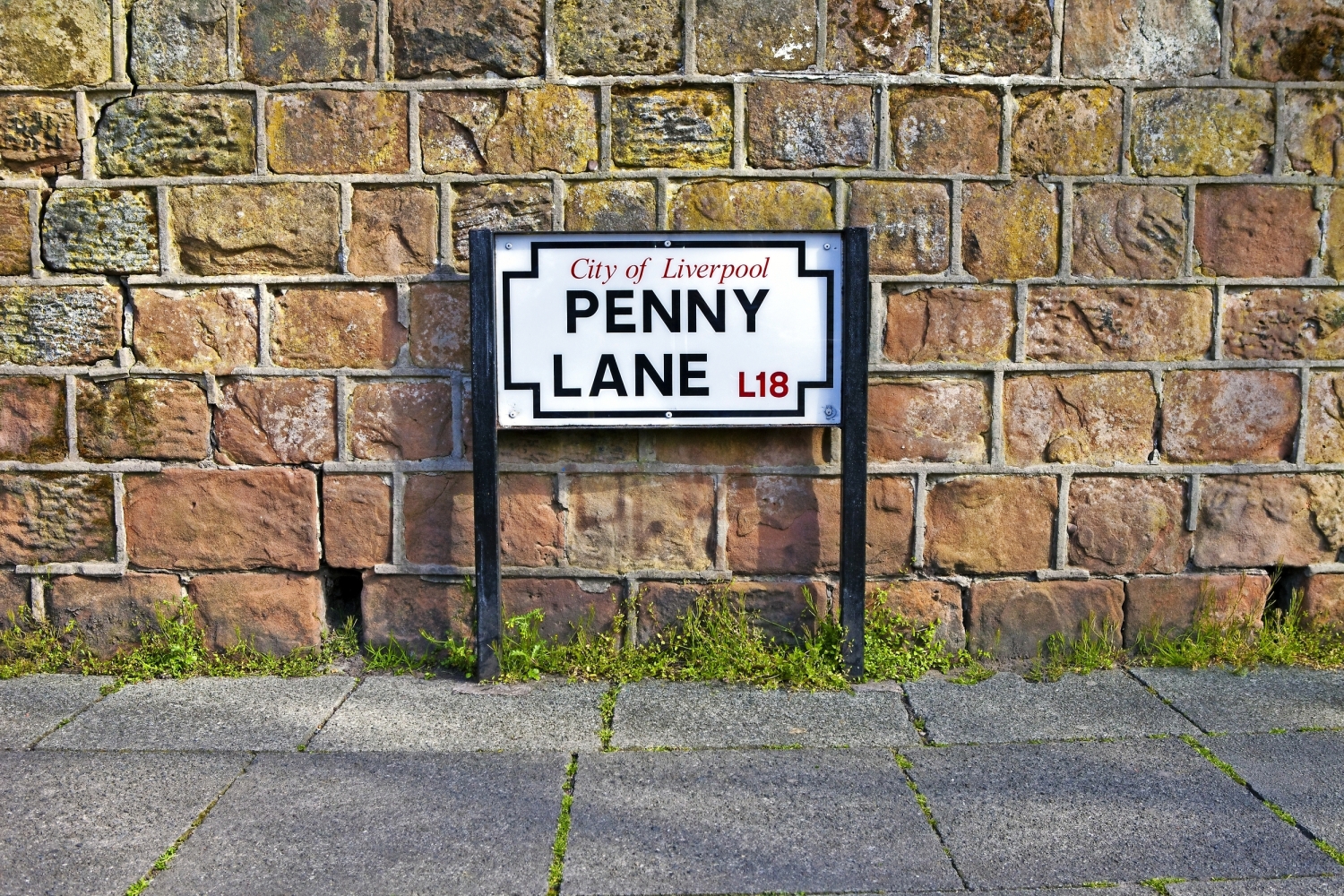 Ein Straßenschild mit der Aufschrift "City of Liverpool Penny Lane L18" vor einer Steinwand.