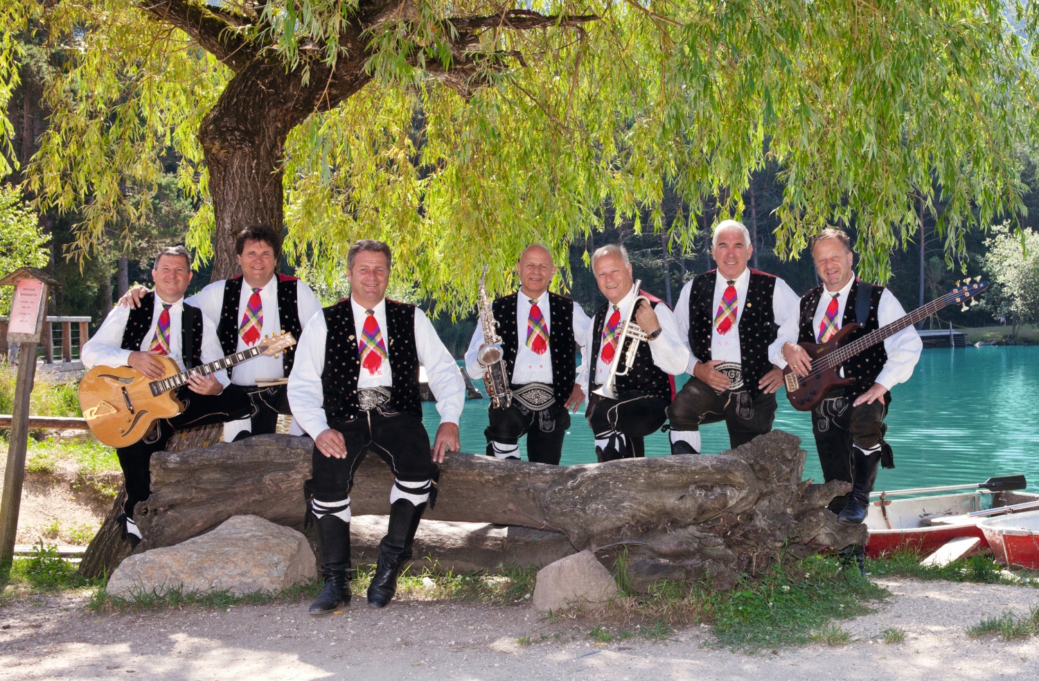 Musikgruppe in traditioneller Tracht posiert vor See und Baum.