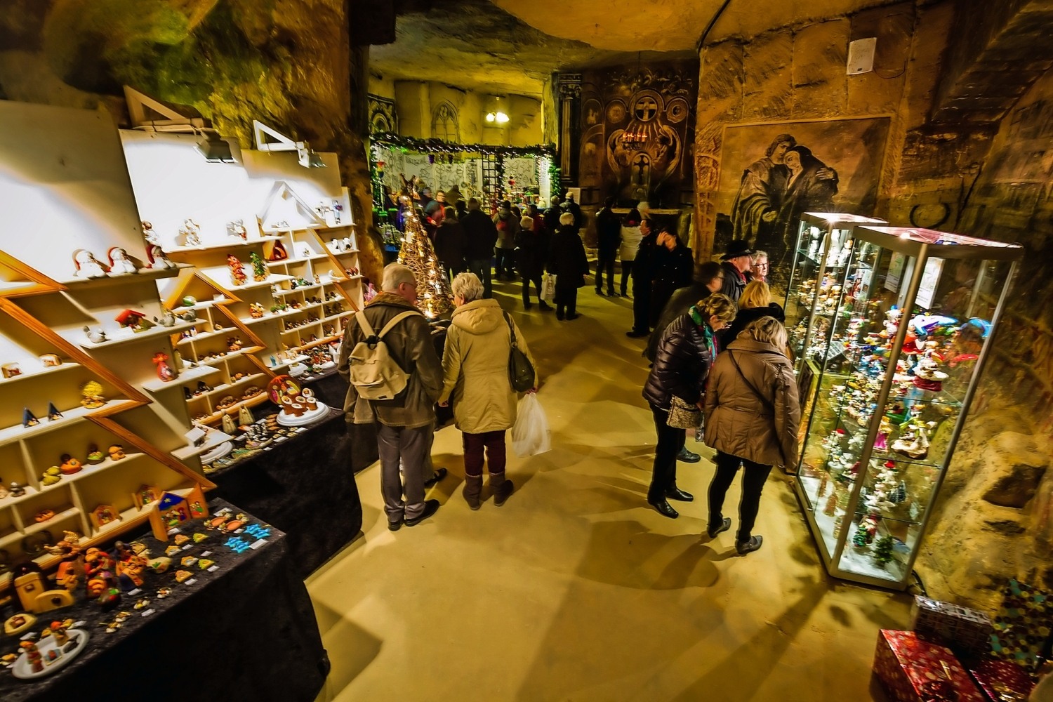 Besucher auf einem Weihnachtsmarkt in einer Höhle mit bunten Ständen und Dekorationen.