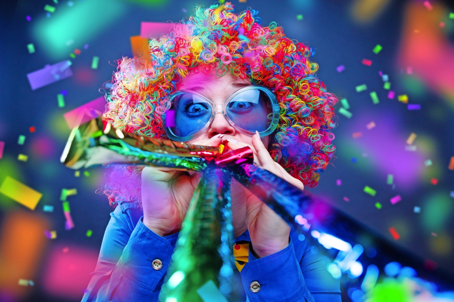 © karepa - stock.adobe.com Person mit bunter Perücke und Blasrohr, umgeben von Konfetti.